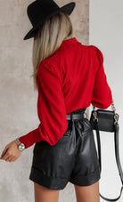Camicia elegante rossa Moda-Mania con colletto asimmetrico, volant e bottoni gioiello, dettaglio di stile raffinato e femminile.