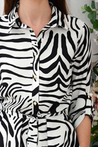 Camicia lunga bianca con fantasia zebrata nera, spacchi laterali e cinturino, modello Moda-Mania, tessuto leggero e elegante.