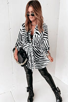 Camicia lunga bianca a fantasia zebrata nera con spacchi laterali e cinturino, camicia Moda-Mania, tessuto leggero e stile elegante.