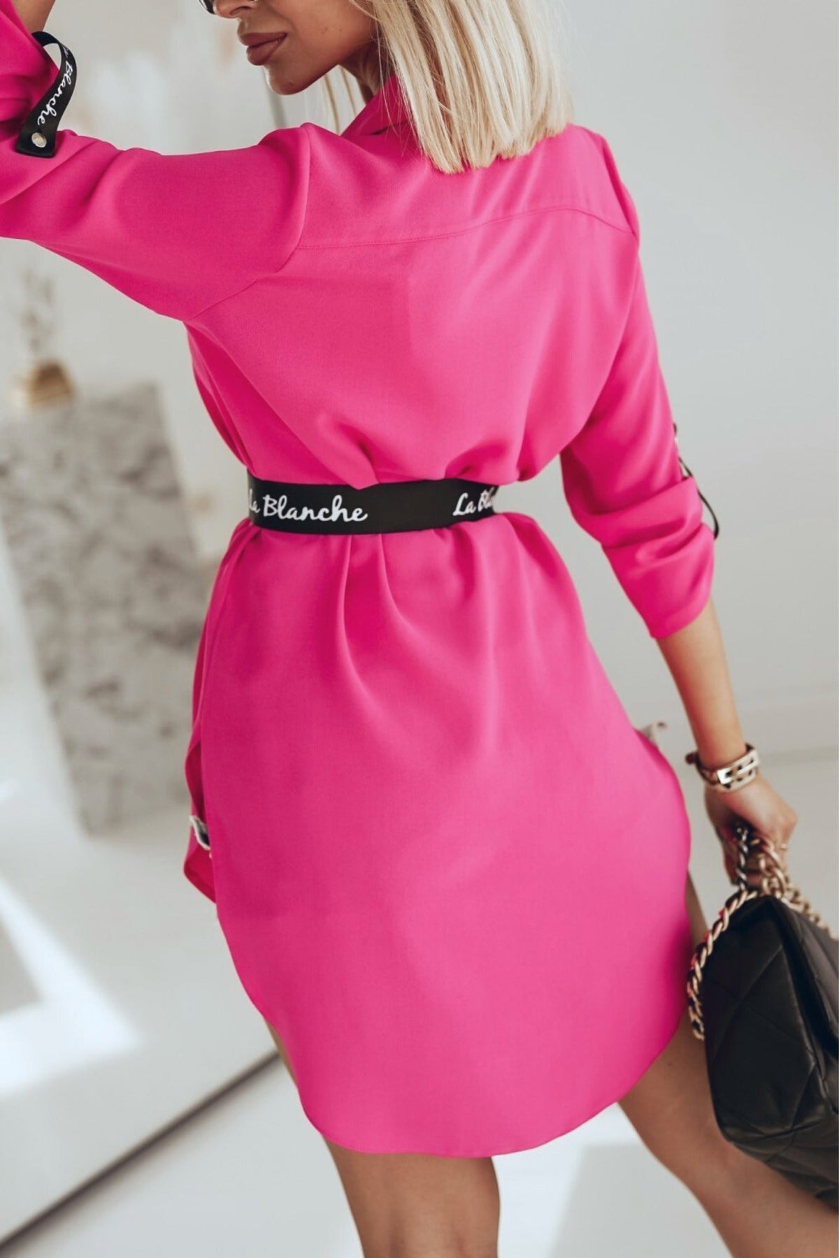 Camicia lunga fucsia Moda-Mania con taglio asimmetrico e cintura nera, dettagli di moda e stile contemporaneo.