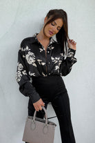 Camicia nera Moda-Mania con fantasia floreale beige, tessuto satinato, taglio comodo e bottoni dorati, vista frontale.