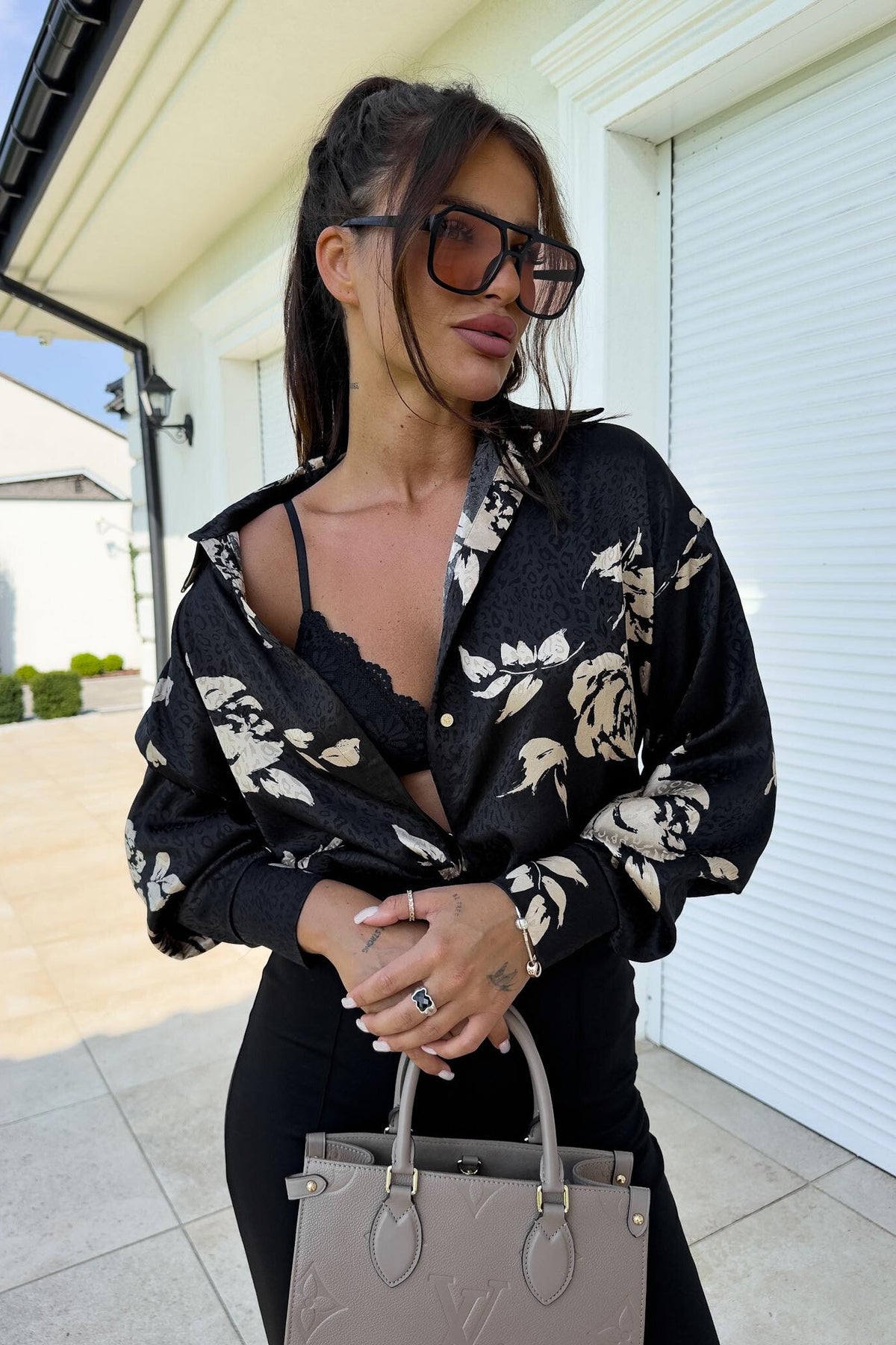 Camicia nera moda-mania con fantasia floreale beige, tessuto satinato, taglio comodo e bottoni dorati, dettaglio visibile.
