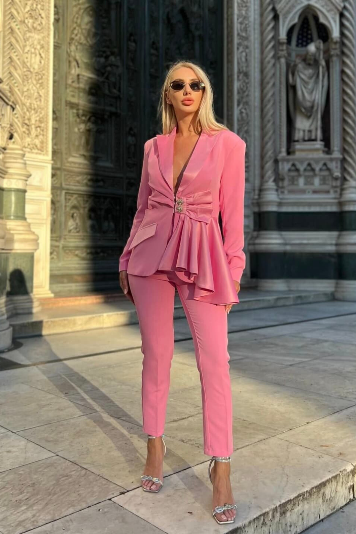 Completo tailleur rosa Bby con giacca e pantalone, bottoni gioiello, volant, fiocco e dettaglio cut-out in vita.