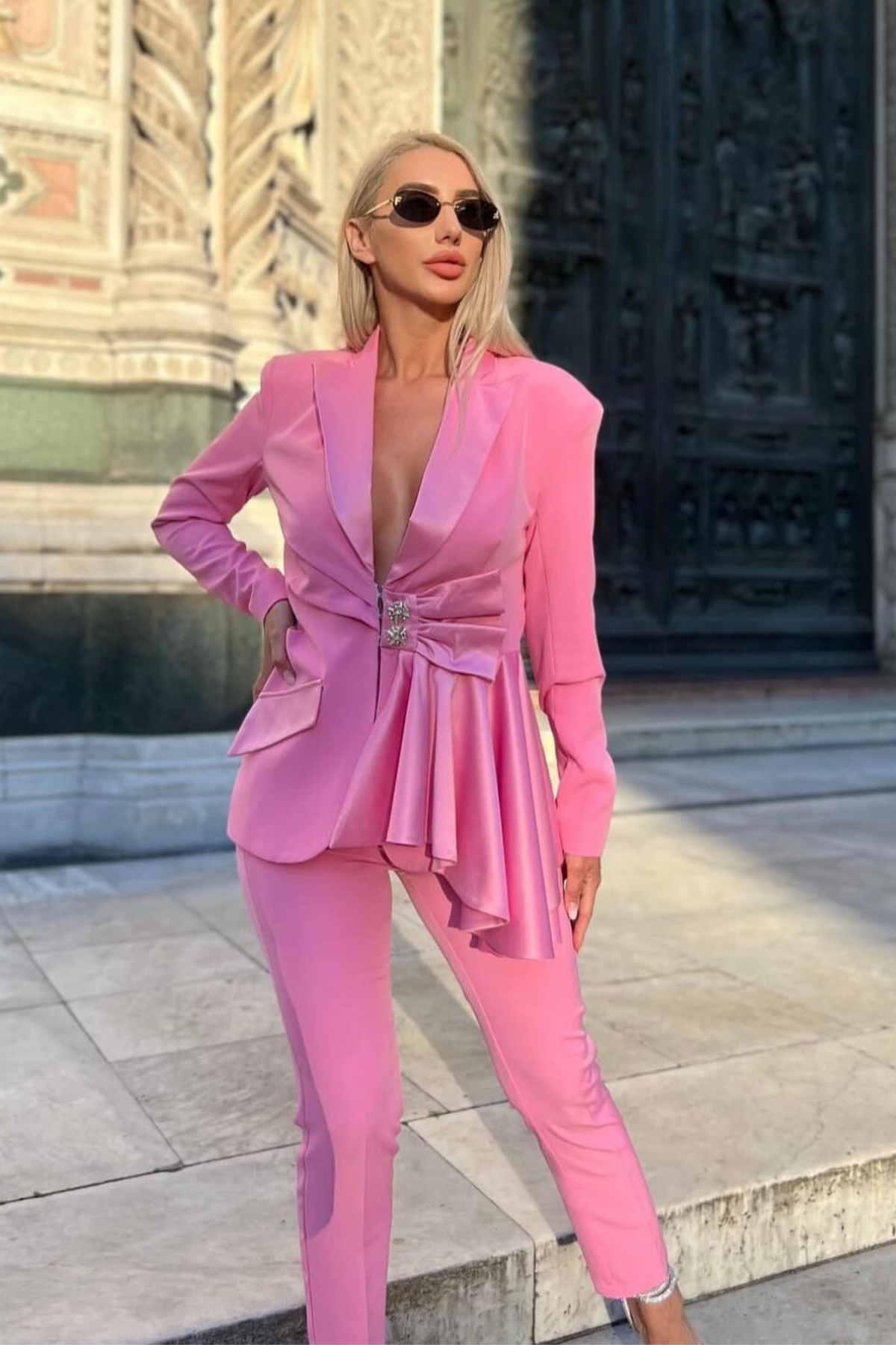 Completo tailleur rosa Bby con giacca e pantaloni, bottoni gioiello, volant, fiocco e dettaglio cut-out in vita.