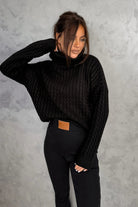 Maglione oversize nero in filato morbido con trecce, collo alto e polsini a coste, di Moda-Mania.