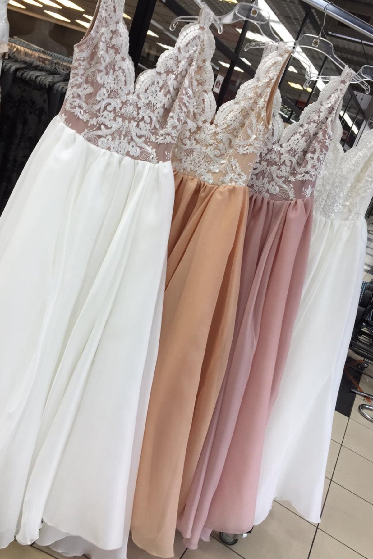 Abito lungo bianco da cerimonia Moda-Mania con corpetto ricamato e gonna ampia in organza su sfondo rosa cipria.