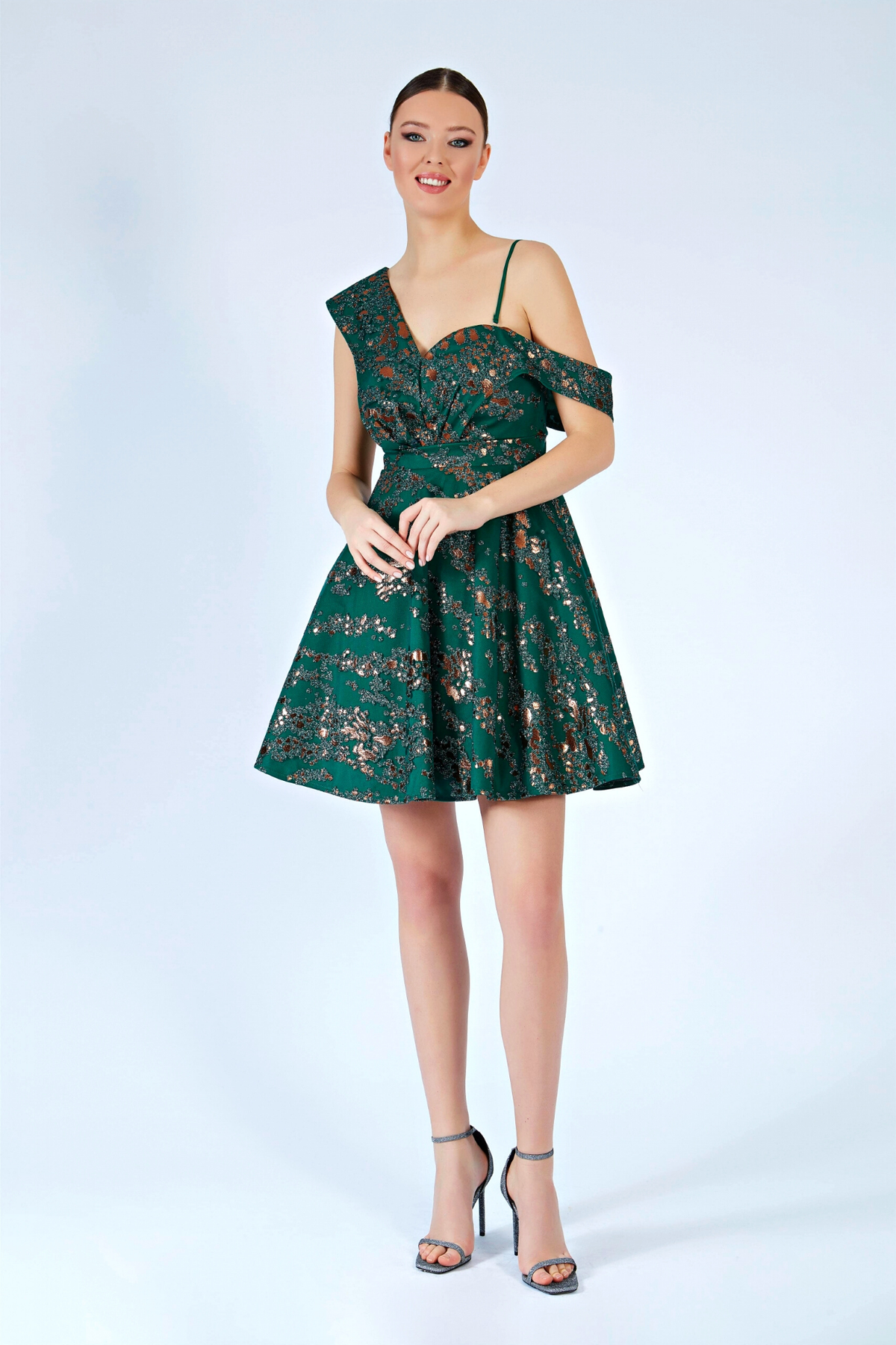 Abito corto svasato verde smeraldo con fantasia glitterata e spalla cadente, firmato Moda-Mania, in tessuto leggero e elegante.
