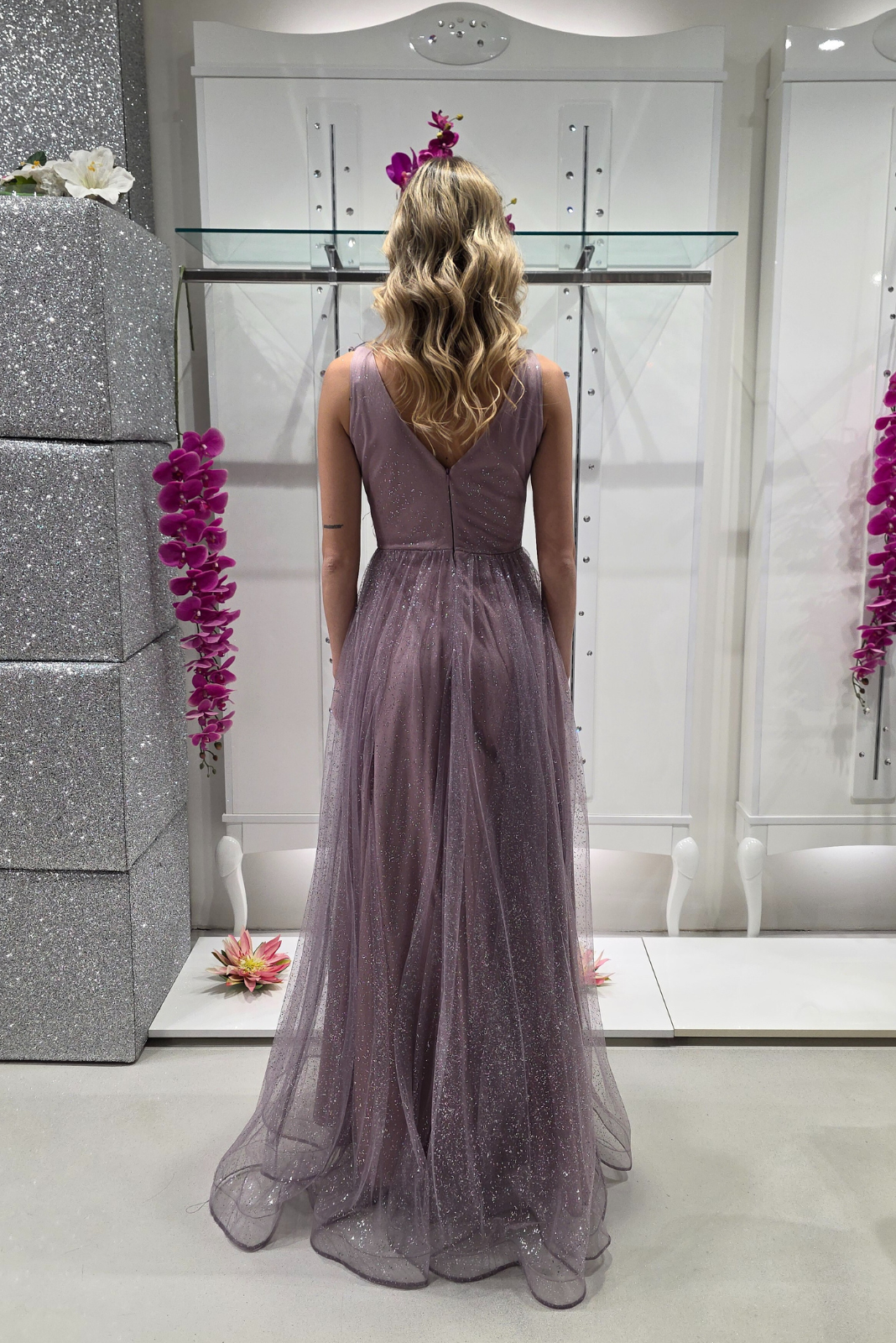 Abito lungo svasato lilla in tulle glitterato con spacco e decorazioni floreali, modello Moda-Mania.
