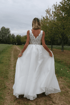 Abito lungo bianco da cerimonia Moda-Mania, svasato con corpetto ricamato e gonna ampia in organza, su sfondo rosa cipria.