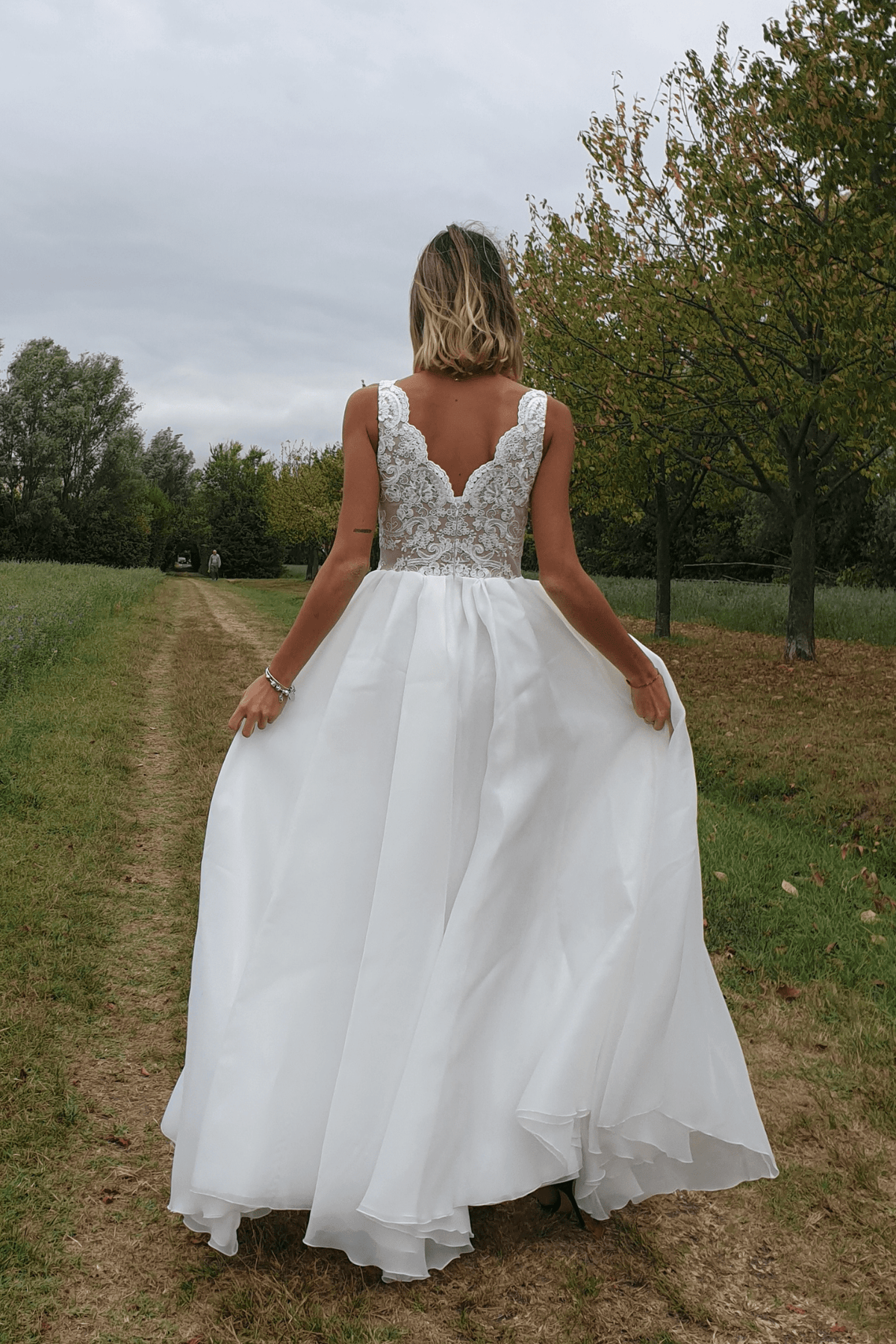 Abito lungo bianco da cerimonia Moda-Mania, svasato con corpetto ricamato e gonna ampia in organza, su sfondo rosa cipria.