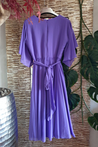Abito svasato donna curvy viola lavanda con maniche a campana, cinturino in vita e accessorio, lungo e elegante.