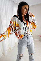 Camicia bianca larga con fantasia astratta arancione, giallo e nero in tessuto satinato lucido con bottoni dorati, marca Moda-Mania.