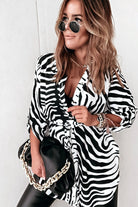 Camicia lunga bianca fantasia zebrata nera con spacchi laterali e cinturino, stile Moda-Mania, tessuto leggero e dettagli eleganti.