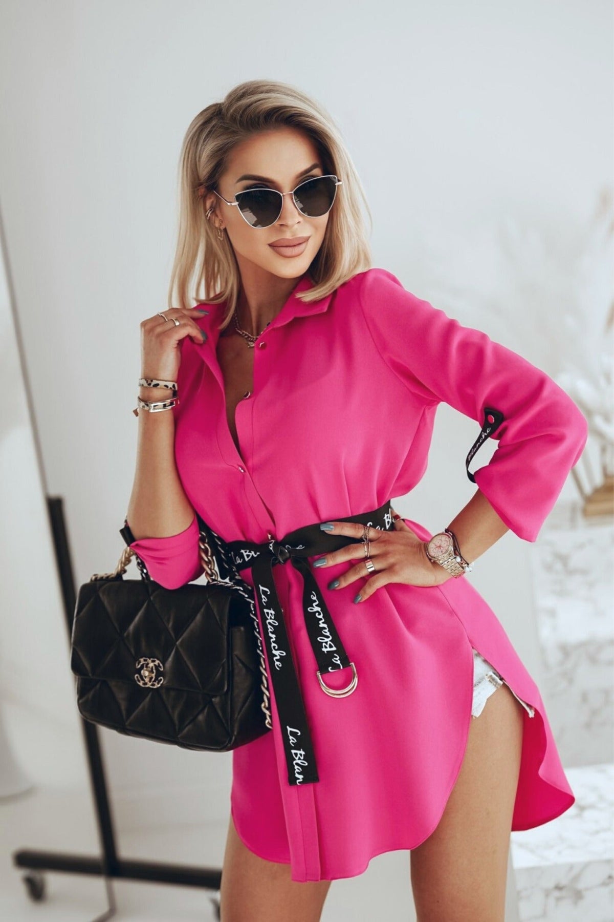 Camicia lunga fucsia Moda-Mania con taglio asimmetrico e cintura nera, dettaglio di moda elegante e moderna.