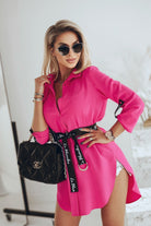 Camicia lunga fucsia Moda-Mania con taglio asimmetrico e cintura nera, dettaglio di moda elegante e moderna.