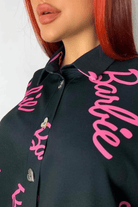Camicia oversize nera Moda-Mania con scritta fucsia Barbie, bottoni a forma di cuore dorato, stile casual e trendy.