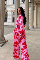 Pantaloni lunghi a palazzo rosa con fantasia di rose rosse, tasche laterali e vita medio alta, firmati Moda-Mania.