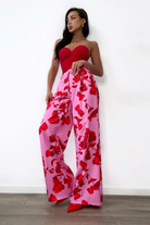 Pantaloni lunghi a palazzo rosa con fantasia di rose rosse, tasche laterali e vita medio alta, firmati Moda-Mania.