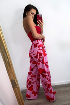 Pantaloni lunghi a palazzo rosa con fantasia di rose rosse, tasche laterali e vita medio alta, marca Moda-Mania.