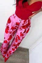 Pantaloni lunghi a palazzo rosa con fantasia di rose rosse, tasche laterali e vita medio alta, firmati Moda-Mania.