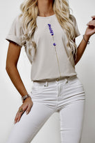 T-shirt beige in cotone elasticizzato con stampa a piccoli fiori lilla e viola, maniche corte con risvolto, Moda Mania.