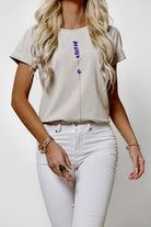 T-shirt beige in cotone elasticizzato con stampa di piccoli fiori lilla viola, maniche corte con risvolto, moda Mania.