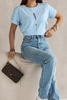T-shirt celeste in cotone elasticizzato con stampa a piccoli fiori lilla e viola, maniche corte con risvolto, moda Mania.