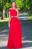 Abito lungo rosso Artista con scollatura a barchetta, fascia floreale in vita e taglio svasato, indossato in un contesto elegante.