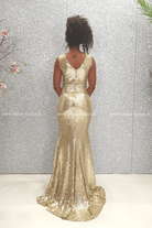 Abito lungo a sirena dorato Chanttal con paillettes, spacco centrale e ricami neri, indossato con dettagli eleganti.