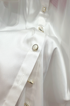 Camicia elegante bianca Moda-Mania in tessuto satinato con maniche a sbuffo e bottoni gioiello, vista frontale.