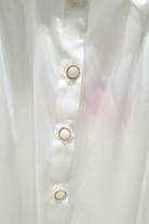 Camicia elegante bianca Moda-Mania in tessuto satinato con maniche a sbuffo e bottoni gioiello, dettaglio frontale.