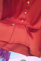 Camicia elegante rossa Moda-Mania in satin, con maniche sbuffo e bottoni gioiello bianchi, dettagli raffinati e tessuto lucido.