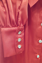Camicia elegante rossa in tessuto satinato con maniche a sbuffo e bottoni gioiello bianchi, moda-mania, dettaglio frontale.